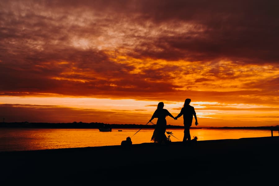 Silhouette of the couple walking their dogs along the shore at sunset on Banksia Beach.