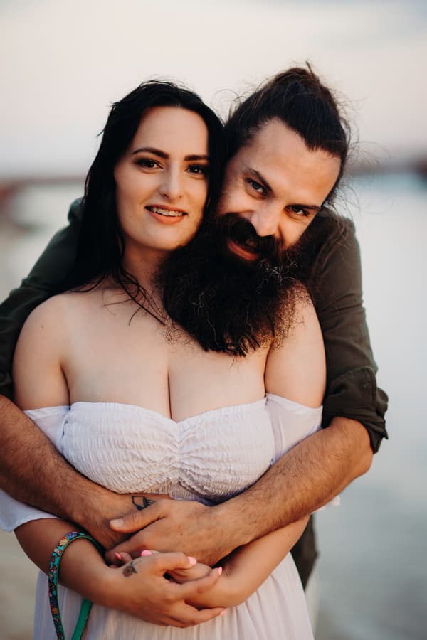 The couple embracing warmly on Woorim Beach, with one person smiling and the other resting their head on their shoulder. The light is soft and warm.
