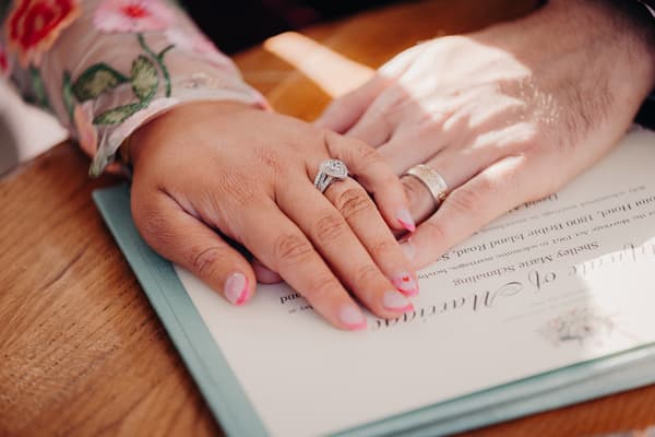 The bride and groom place their hands together on a wedding certificate, showing their wedding rings. Marriage equality Australia by She Said Yes.
