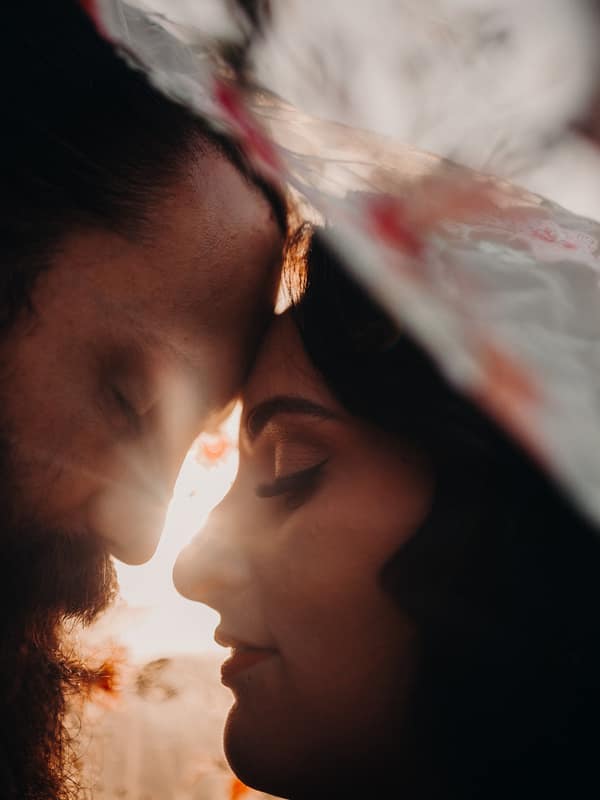 The bride and groom at Sandstone Point Hotel in a close-up couple portrait with their foreheads touching, backlit by sunlight and partially covered by a translucent veil.