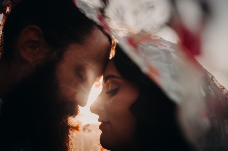 The bride and groom at Sandstone Point Hotel in a close-up couple portrait with their foreheads touching, backlit by sunlight and partially covered by a translucent veil.