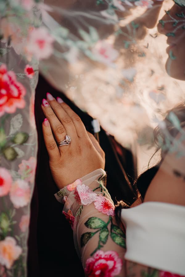 The bride and groom share an intimate moment at Sandstone Point Hotel, with the bride's hand adorned with a wedding ring resting on the groom's chest, partially obscured by a floral embroidered veil.