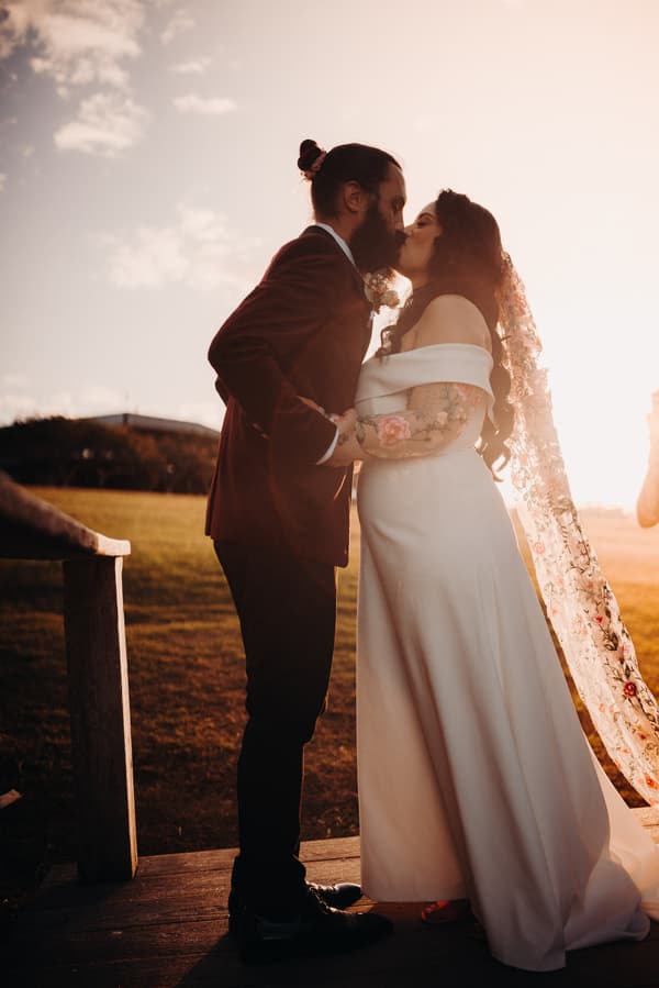 The bride Mindy and groom David share a kiss during their couple portraits session at Sandstone Point Hotel, with the sun setting behind them.
