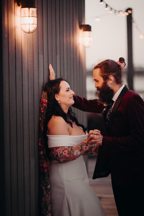 The bride Mindy and the groom David pose together near a wooden wall with warm wall lights at Sandstone Point Hotel during their couple portraits session.