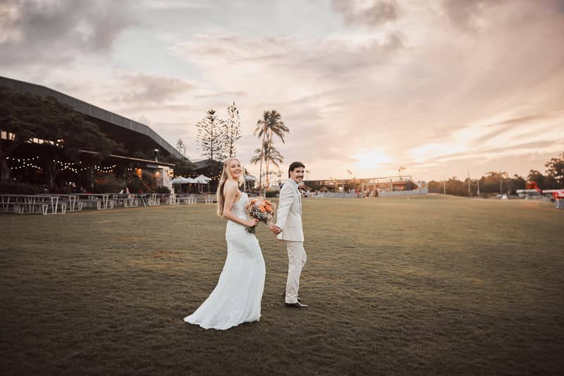 Morgan the bride and Joel the groom hold hands and walk on the grass outside Sandstone Point Hotel during a sunset couple portrait session.