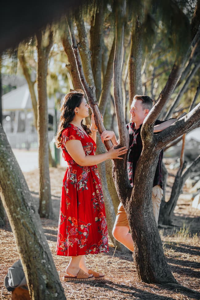 The couple stands among trees at Redcliffe, engaged in conversation with sunlight filtering through.