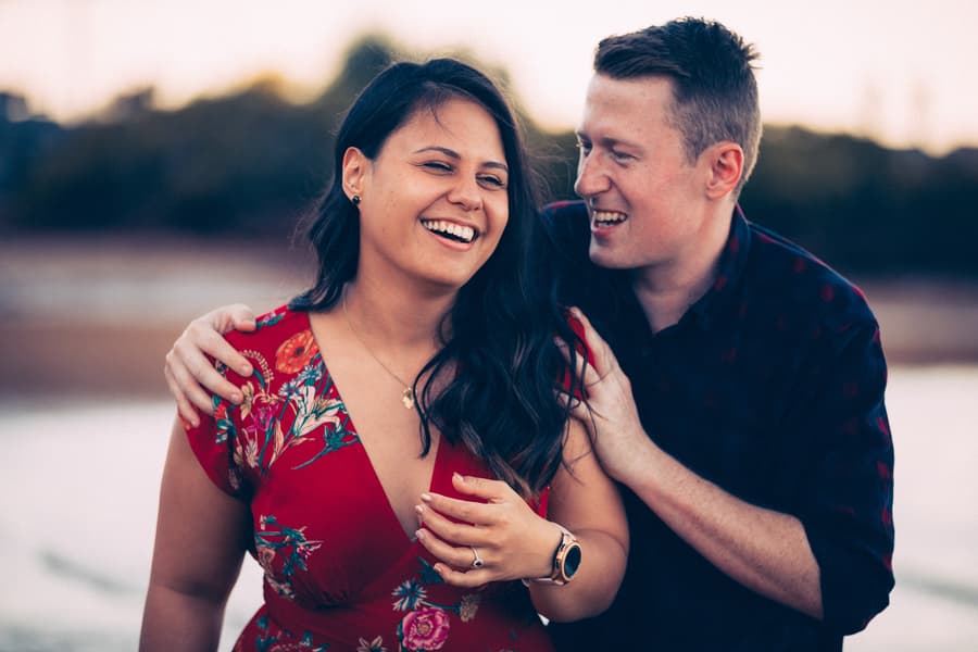 Couple laughing together, the woman wearing a floral dress, with a blurred natural background.