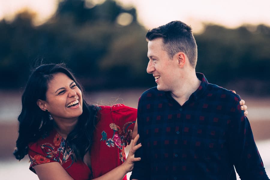 Couple playfully interacting, smiling at each other with a blurred background of trees.