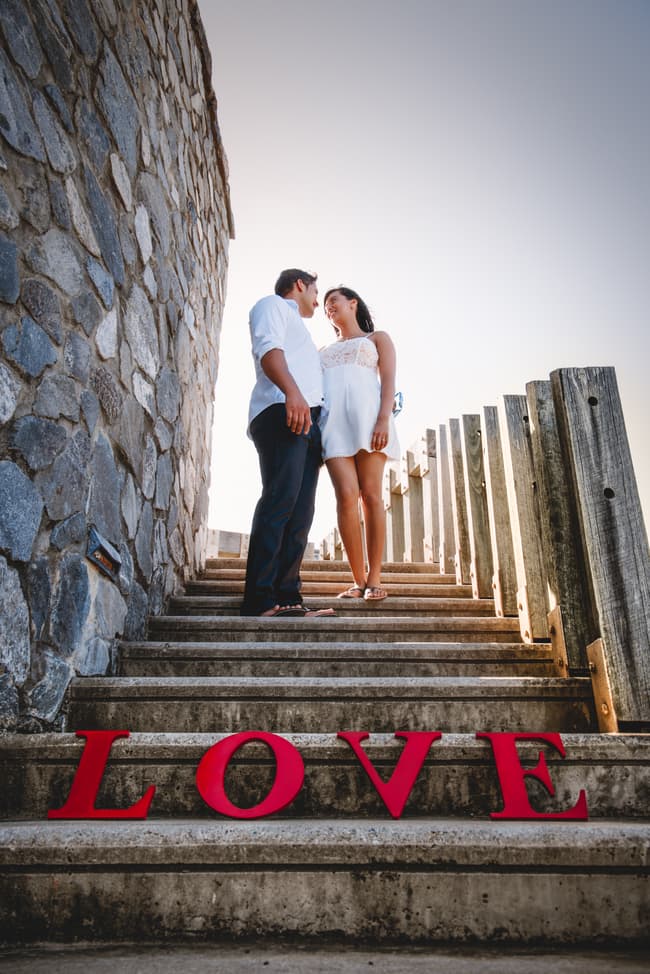 The couple standing on stone steps, looking at each other with 'LOVE' letters on the steps.