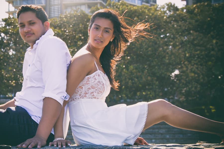 The couple sitting back to back on a stone wall, with wind blowing their hair and trees behind.