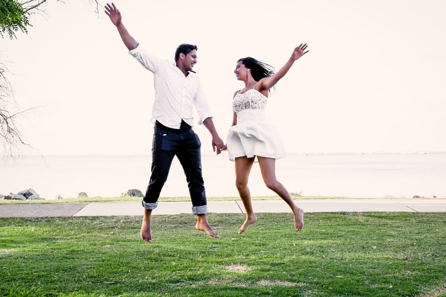 The couple joyfully jumping in the air on grass by the sea at Scarborough Beach.