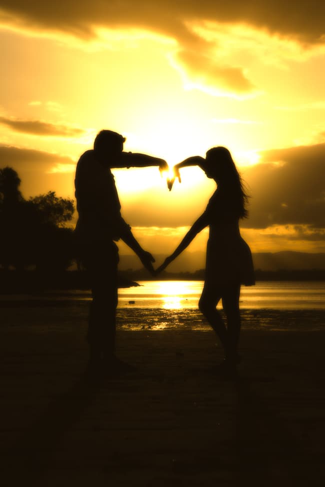 Silhouette of the couple forming a heart shape with their arms at sunset on Scarborough Beach.