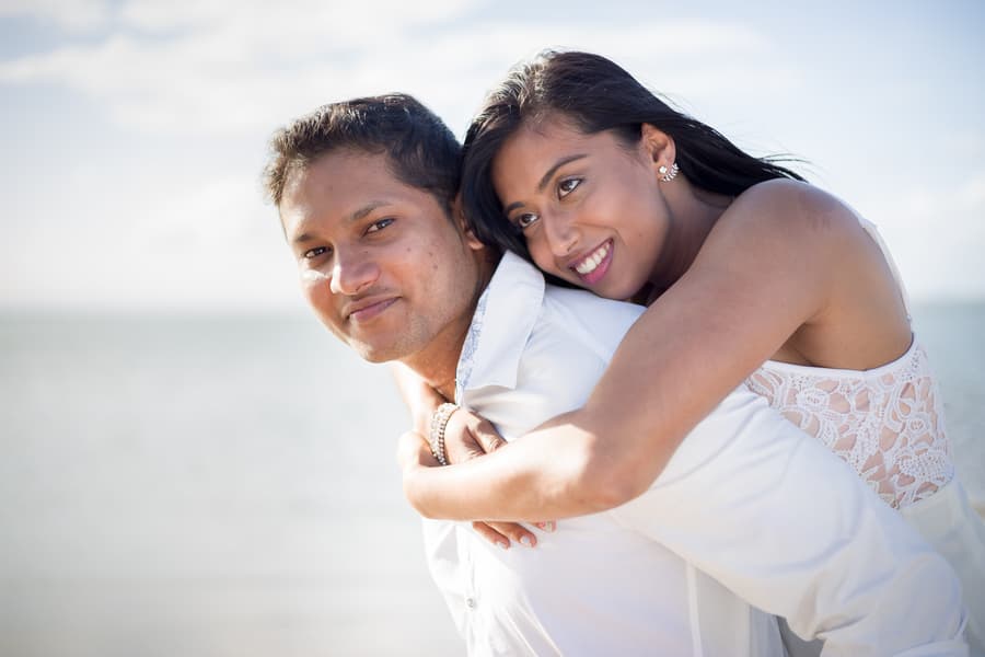A person gives a piggyback ride to another on Scarborough Beach, both smiling brightly.