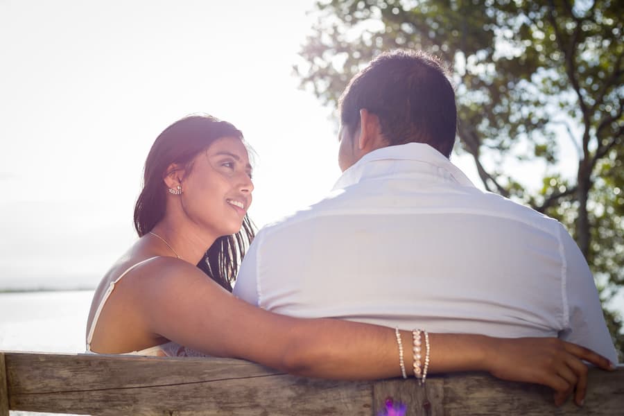 A couple sits on a bench at Scarborough Beach, with one person looking at the other lovingly.