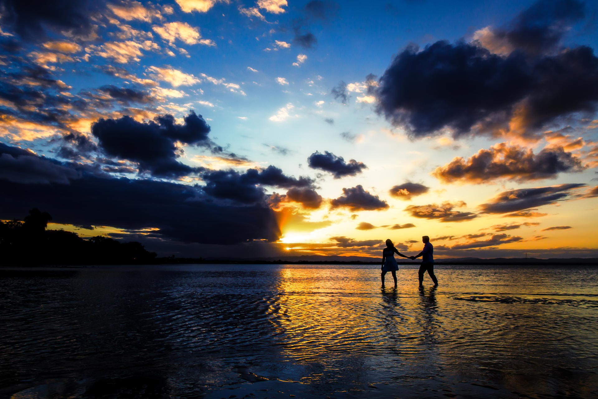 The couple walking hand in hand in shallow water at Scarborough Beach during a vibrant sunset.