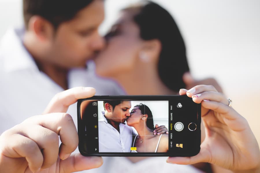 A close-up of a phone capturing a couple kissing, with the couple blurred in the background.