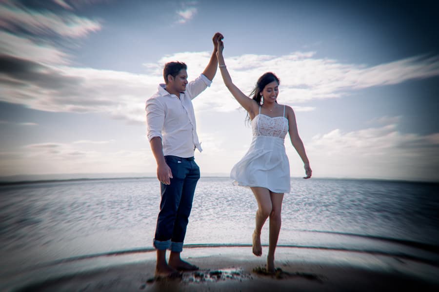 A couple dances playfully on the shore of Scarborough Beach, with the sea in the background.