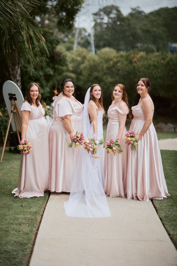 Olivia the bride stands with four bridesmaids in pale pink dresses holding bouquets at Eatons Hill Hotel during the couple portraits stage.