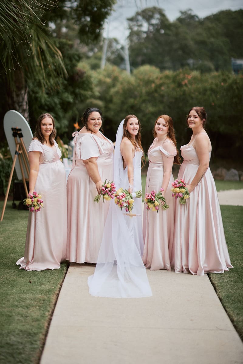 Olivia the bride stands with four bridesmaids in pale pink dresses holding bouquets. Wedding photographer Brisbane by She Said Yes.