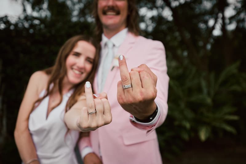 Olivia the bride and Jake the groom at Eatons Hill Hotel show their wedding rings on their middle fingers in a close-up portrait.