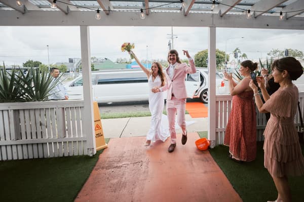 Olivia and Jake enter the reception area at White Horse Ranch, with Olivia holding a bouquet and guests taking photos and applauding.