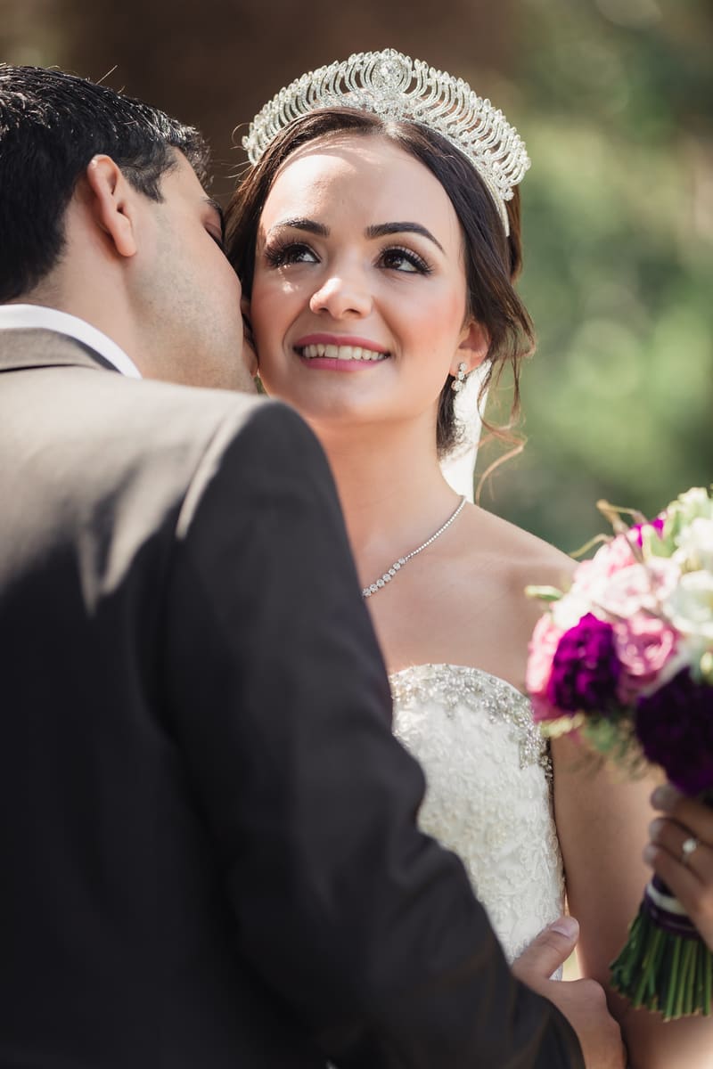 Pasha kisses Maryam on the cheek as she smiles, holding a bouquet of flowers. Engagement photography Brisbane by She Said Yes.