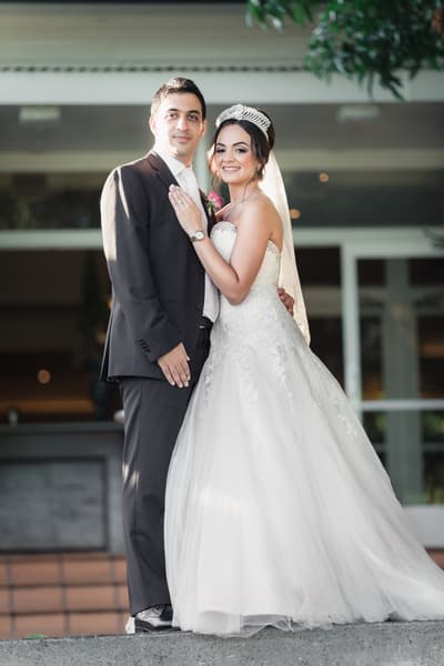 The bride Maryam in a white wedding gown and tiara stands next to the groom Pasha in a dark suit and light tie, posing together outside. Wedding photographers Brisbane by She Said Yes.