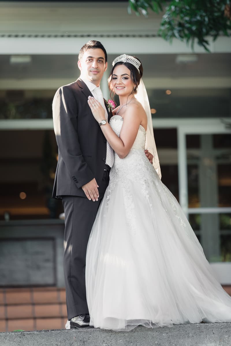 The bride Maryam in a white wedding gown and tiara stands next to the groom Pasha in a dark suit and light tie, posing together outside. Brisbane elopement photographer by She Said Yes.