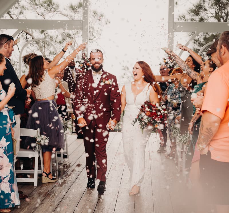 Red and Jayden walk down the aisle at Sandstone Point Hotel — The Pavilion as guests throw confetti.