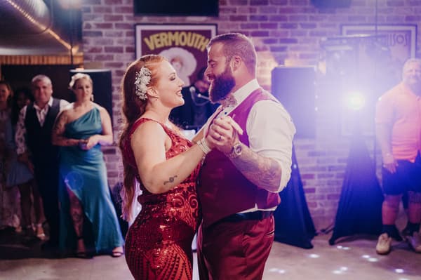 The bride Red and groom Jayden dance together on the reception stage at Sandstone Point Hotel — The Cellar, while guests watch in the background.