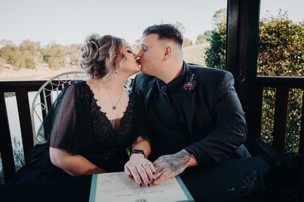 Bride Renae and groom Adam share a kiss while seated at a table with a certificate during their ceremony. Brisbane wedding photographers by She Said Yes.