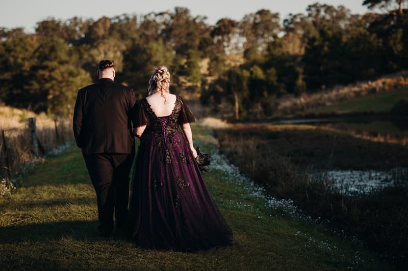 Renae and Adam walk arm in arm along a grassy path beside a pond at Ocean View Estates during their couple portraits session.