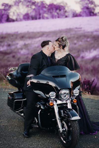 Renae and Adam kiss while seated on a black motorcycle. Best Brisbane wedding photographer by She Said Yes.