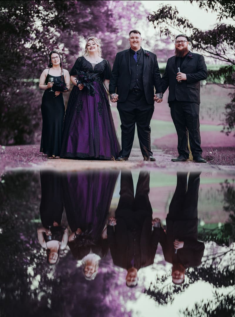 Renae the bride in a purple and black gown and Adam the groom in a black suit stand holding hands outdoors, one holding a wine glass and the other holding a bottle, reflected in a pool of water in front of them. Asian wedding photographer by She Said Yes.
