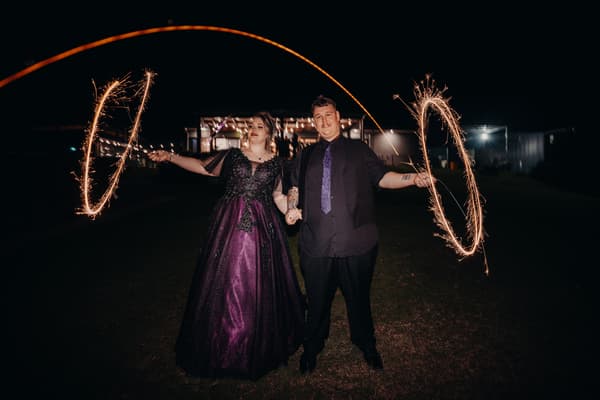 The bride Renae and groom Adam stand outside Ocean View Estates — Function Room at night holding sparklers creating light trails.