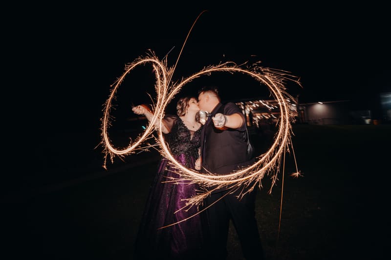 The bride Renae and groom Adam kiss while holding sparklers at night outside Ocean View Estates — Function Room during the reception.