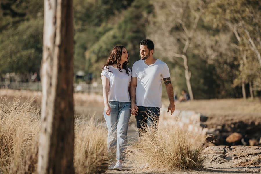 The couple walks hand in hand through a grassy path at Kangaroo Point, smiling at each other.