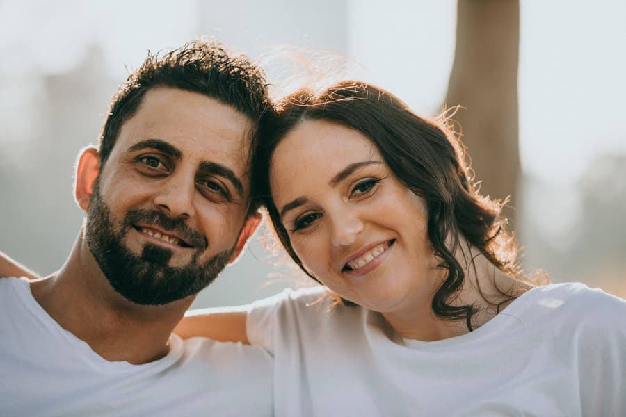 Close-up of the couple smiling warmly at the camera, sitting closely together in natural light.