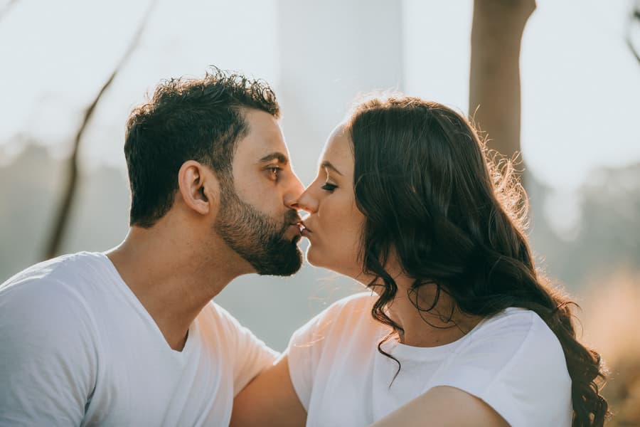 The couple shares a gentle kiss while sitting closely, with soft light illuminating their faces.