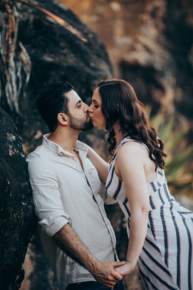 The couple sharing a kiss while leaning against a rock at Kangaroo Point, surrounded by natural scenery.