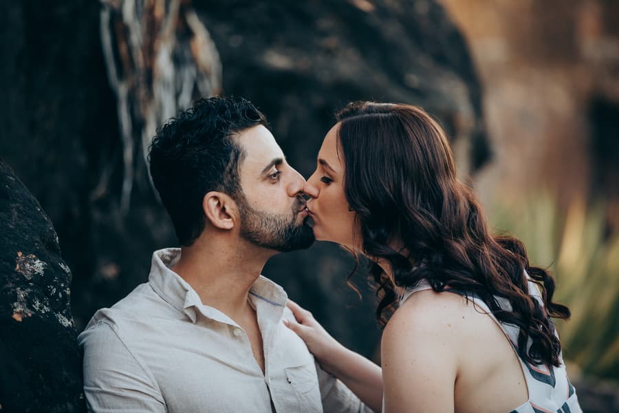 The couple sharing a gentle kiss, with the natural backdrop of rocks and greenery at Kangaroo Point.