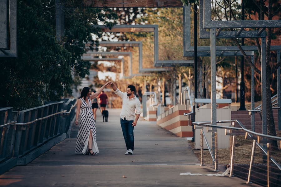 The couple dancing on a bridge at Kangaroo Point, surrounded by trees and geometric structures.