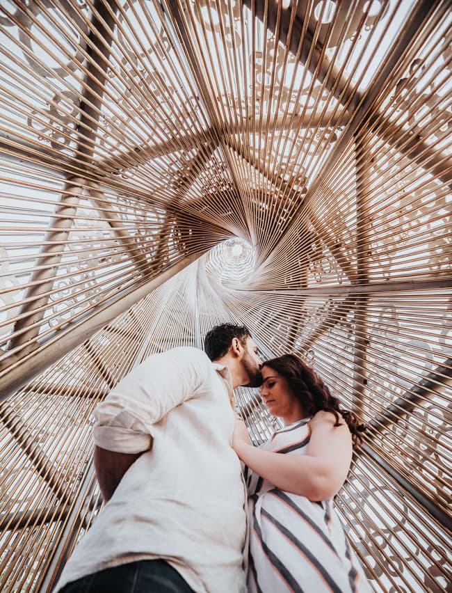 The couple standing under an intricate metal structure, sharing an intimate moment at Kangaroo Point.