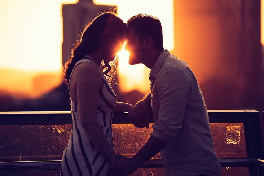 The couple leaning in for a kiss at sunset, with warm light creating a romantic atmosphere at Kangaroo Point.