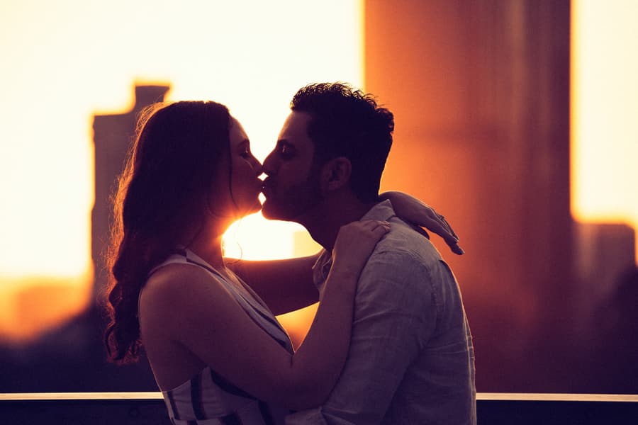 The couple shares a kiss at sunset with a city skyline in the background at Kangaroo Point, Brisbane.
