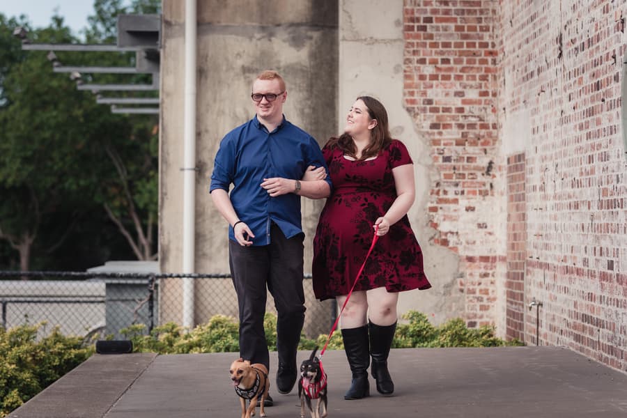 The couple walks arm in arm with their two dogs, against a backdrop of brick walls at Brisbane Powerhouse.