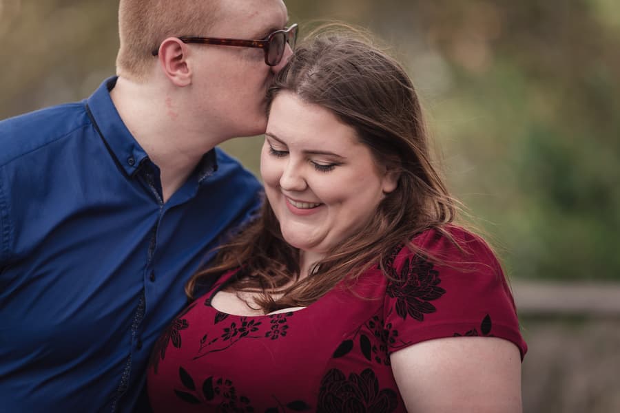One person kisses the other's forehead tenderly, both smiling softly with a blurred background.
