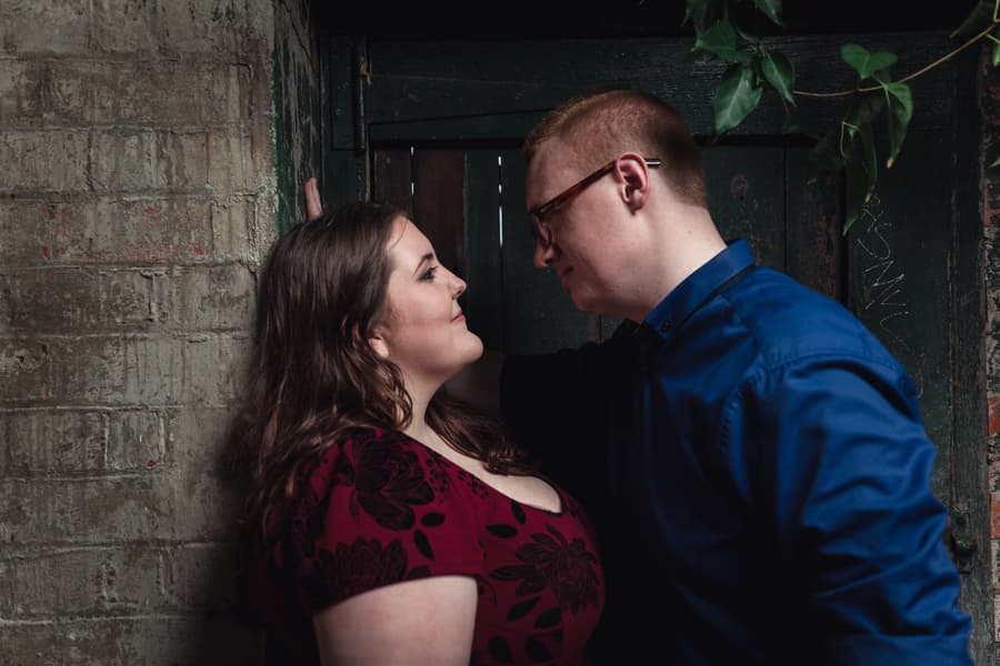 The couple stands close in an intimate pose against a textured wall at Brisbane Powerhouse, gazing into each other's eyes.