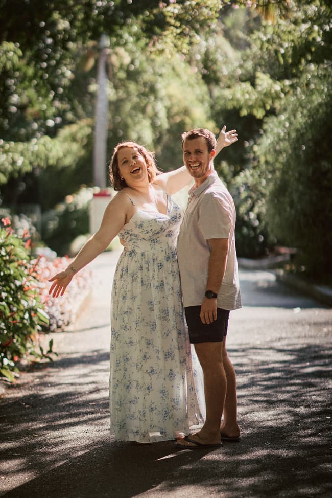 The couple joyfully poses on a sunlit path at Brisbane Botanic Gardens, arms wide open.