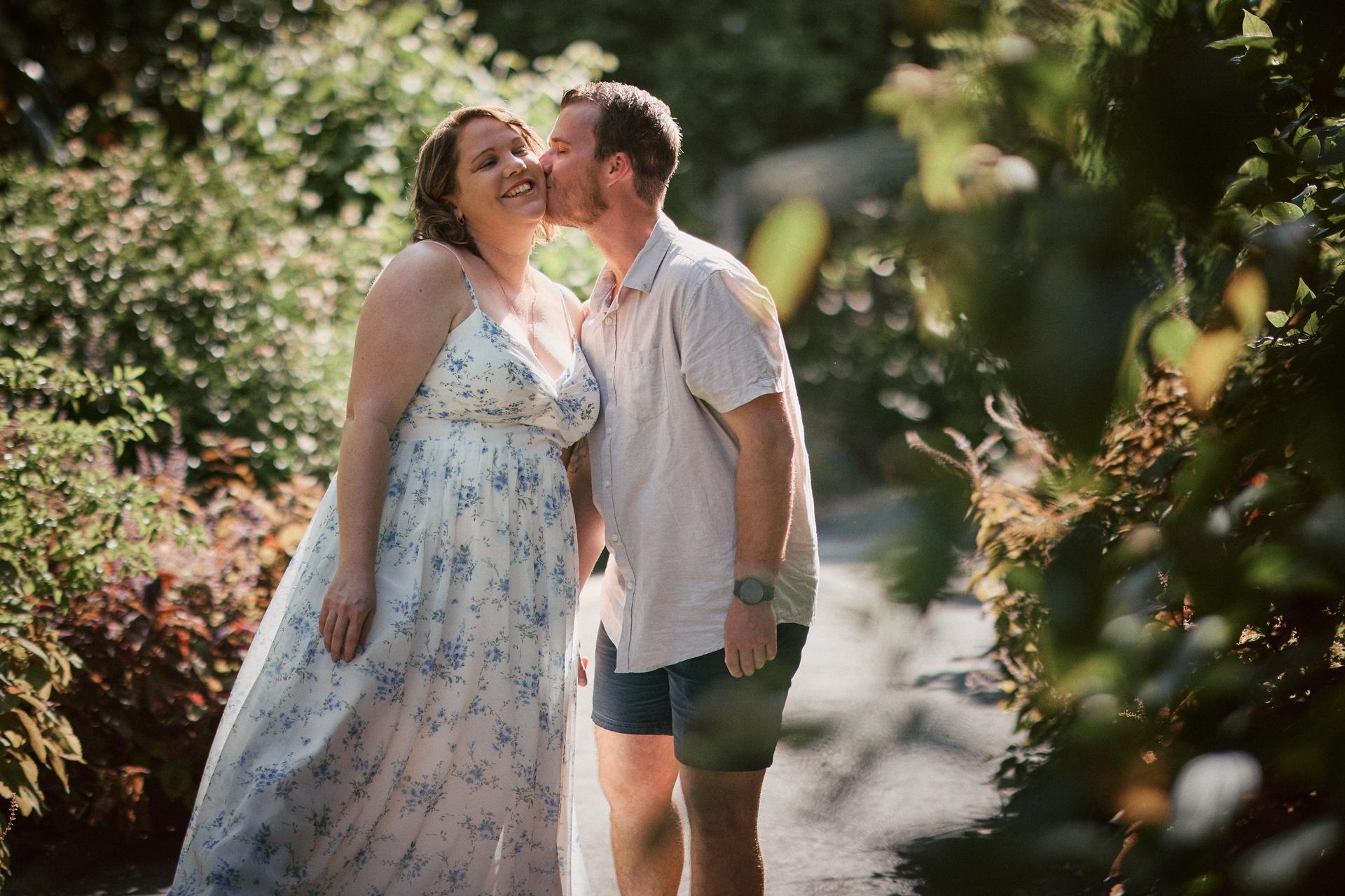 The couple shares a playful kiss surrounded by lush greenery at Brisbane Botanic Gardens.